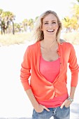 A blonde woman wearing a pink top, a cardigan and jeans on the beach