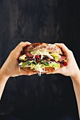 Hands holding a roast beef, lettuce and cheese sandwich