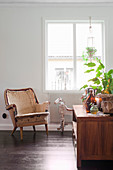 Vintage armchair and three-wheeled horse below window with houseplant on sideboard in foreground