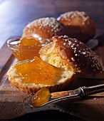 A knife next to a brioche, sliced open, with coarse sugar crystals and apricot jam