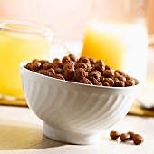 A bowl of cereal chocolate balls and orange juice