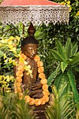 Buddha statue decorated with garland of flowers below Balinese parasol