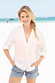 A blonde woman wearing a white blouse and denim shorts on the beach