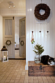 Cat sitting on wooden trunk in country-house-style hallway with double doors and winter decorations