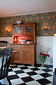 Old dresser against wall with wooden wainscoting and patterned wallpaper