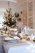 Stimmungsvoll gedeckter Tisch mit Nadelzweigen und Lichterkette an Weihnachten