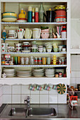 Retro crockery on kitchen shelves with lace trim above sink