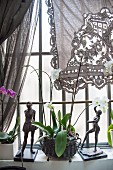 Two sculptures and orchid on windowsill below lace curtain