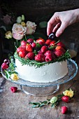 A vanilla buttercream cake garnished with red fruits and rosemary