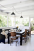 Black dining table with old church bench and chairs in light-flooded dining area