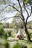 Mother and daughter sit in the hanging chair in the garden