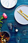 Gold cutlery on plate, glasses, salt and pepper shakers and flowers on table