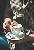 Mann trinkt Tasse Cappuccino in sonnigem Strassencafe