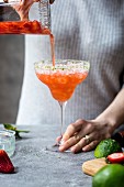 A woman is pouring margarita into a margarita glass full of crushed ice