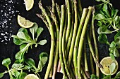 Bundle of young raw uncooked organic green asparagus with green salad leaves, sliced lemon and sea salt