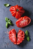Whole and sliced organic tomatoes Coeur De Boeuf with pink salt and basil on blue gray metal texture background