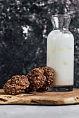 Chocolate zucchini oatmeal cookies leaned against a bottle of iced milk standing on a wooden board