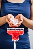 A woman with a blue T-shirt pouring the ice cubes in her hands into watermelon margarita