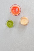 A green smoothie, lemon juice, and blood orange juice in glasses (top view)