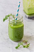 A green wild herb smoothie with a straw in a glass