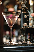 Gin-Cocktail im Martiniglas, garniert mit rosa Orchidee, in einer Bar