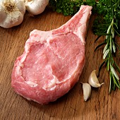 One raw Veal Chop with herbs and garlic on cutting board
