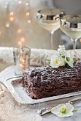 A festive chocolate log decorated with white flowers on a silver serving platter