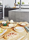 Pizza und Käseplatte auf Holztisch, im Hintergrund Kücheninsel in Anthrazit-Optik