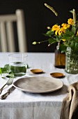 Tisch gedeckt mit Teller, Besteck, Wasserglas und gelbem Blumenstrauss