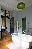 Bathtub in large bathroom with herringbone parquet floor and wrought iron door
