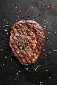 A grilled beef steak with spices on a black background (top view)
