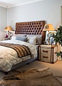 Bed with leather headboard, steamer trunk used as bedside table and animal-skin rug in bedroom