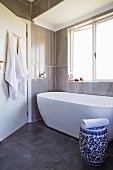 White bathtub and blue and white ceramic drum stool in modernised bathroom