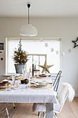 Table festively set in white in front of small Christmas tree on window sill