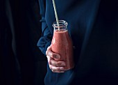 A woman holding a bottle of red smoothie (vegan)