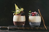 Various dessert breakfast layered chia seeds, chocolate pudding, rice porridge in glass decorated by fresh blackberries, sliced pear, cocoa powder
