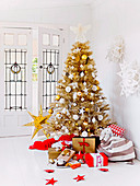 Wrapped gifts around golden Christmas tree in front of the glass door