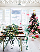 Festlich gedeckter Tisch mit Blumengirlande und geschmückter Weihnachtsbaum