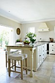 Elegant island counter and white bar stools on large stone flags in kitchen