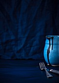 A jug of chocolate sauce and a knife and fork against a dark background