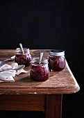 Raspberry jam in three screw top glass jars on a wooden table