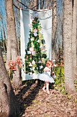 Christmas tree printed on fabric hung between bare trees and little girl wearing white tutu
