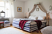 Blue-and-white chequered box spring bed in bedroom with striped wallpaper