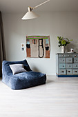 Blue velvet easy chair next to child's painting and chest of drawers