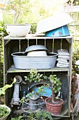 Vintage Holzregal mit verschiedenen Emailleschüsseln, Zinkwanne und Bonsaibäumchen in Garten