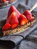 Slice of gluten free chocolate tart served with fresh strawberries
