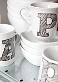 weiße Tassen mit schwarz schraffierten Buchstaben