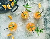 Erfrischender Sommercocktail mit Orangen, Pfefferminze und Crushed Ice in Gläsern (Aufsicht)