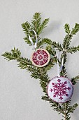 Two hand-made embroidered snowflake decorations on green fir branch