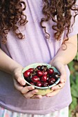 A young girl holding a bowl of fresh cherries